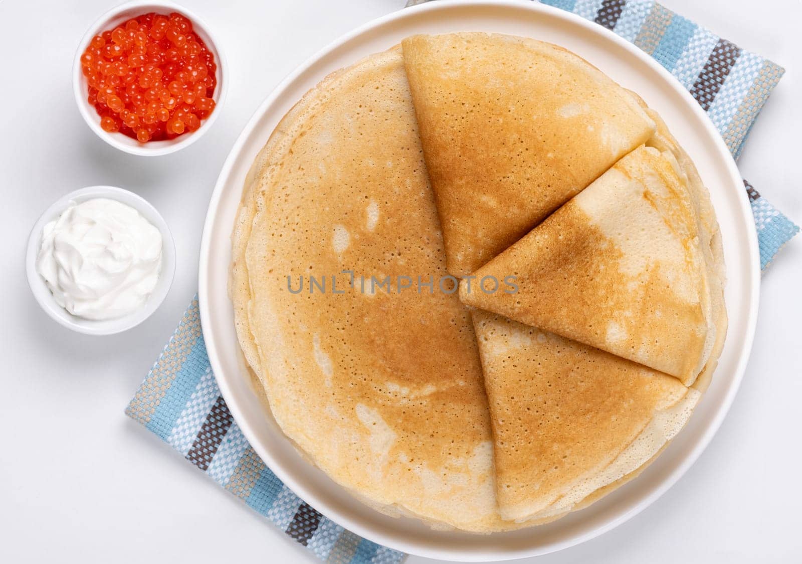 Pancakes with red caviar and sour cream, Close-up of pancakes stacked on white background.