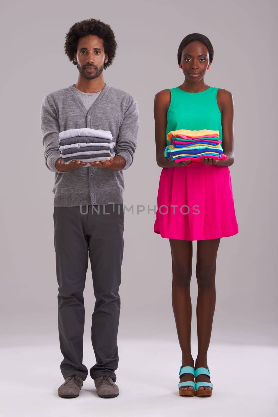 Portrait, couple and folded clothes for laundry, fashion and cleaning in studio isolated on a gray background. African man, serious woman and fabric for housework, housekeeping or chores together.