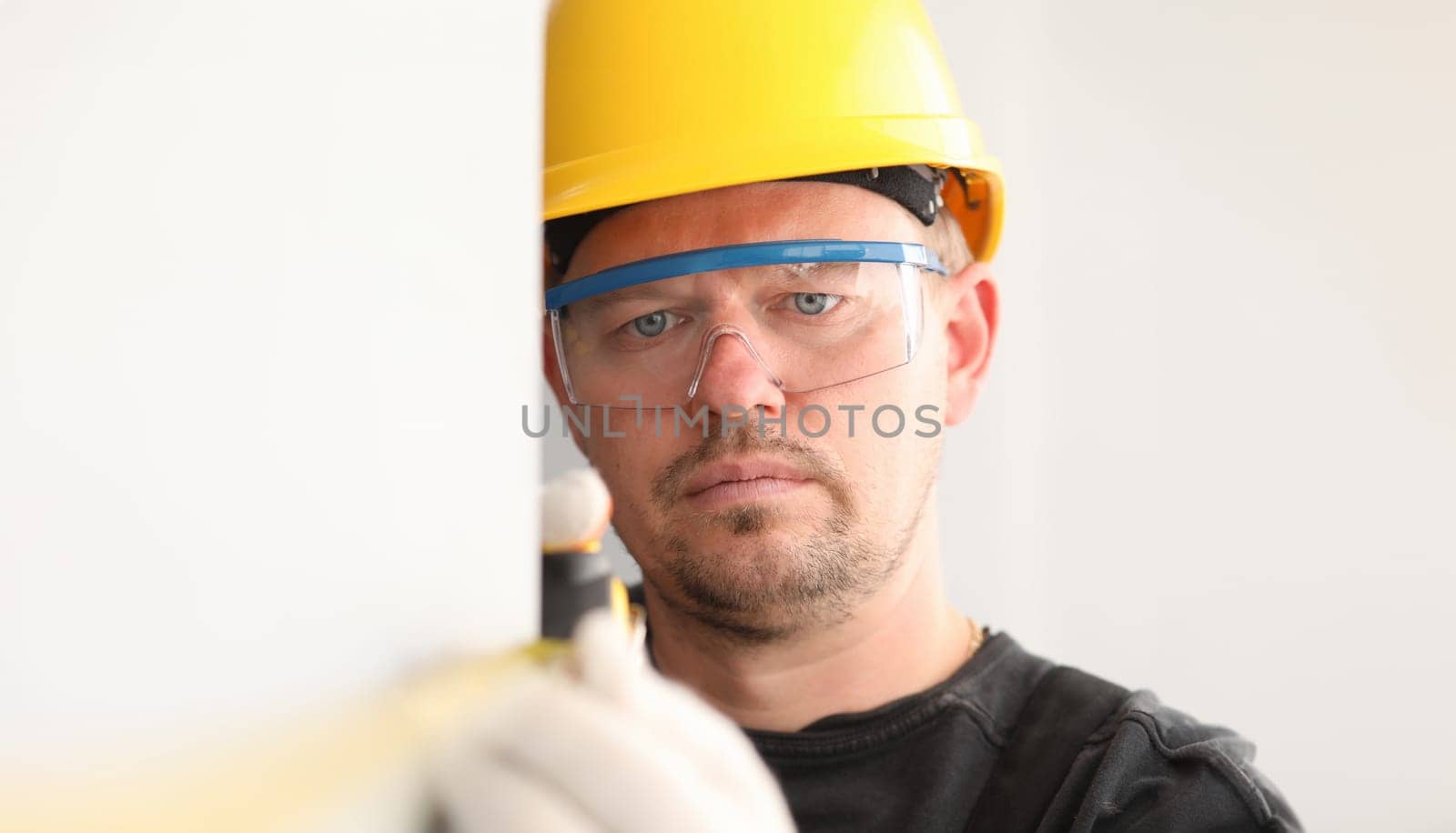 Repairman in helmet and mask, measures tape measure by kuprevich