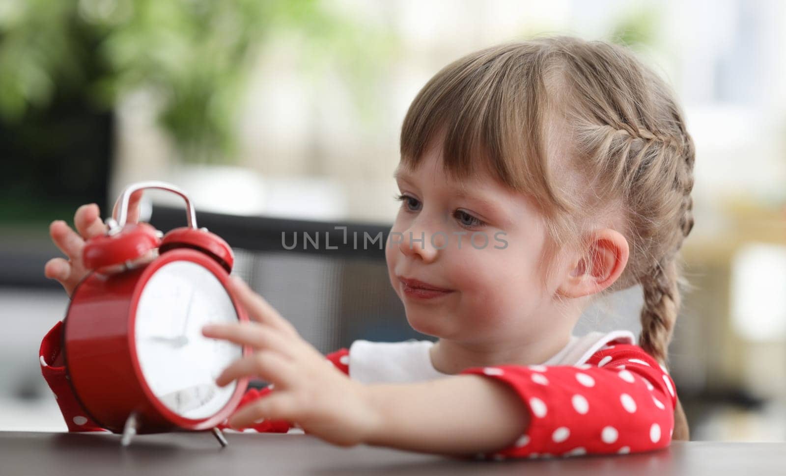 Girl holds alarm clock, carefully looks details. Girl receives knowledge about various objects and phenomena. Entertaining and exciting activity. Determine time on clock with an arrow