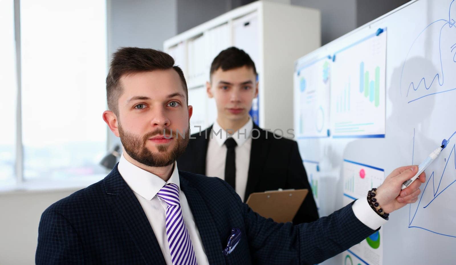 Smiling handsome bearded caucasian man in office telling something important while showing information on white board headshot