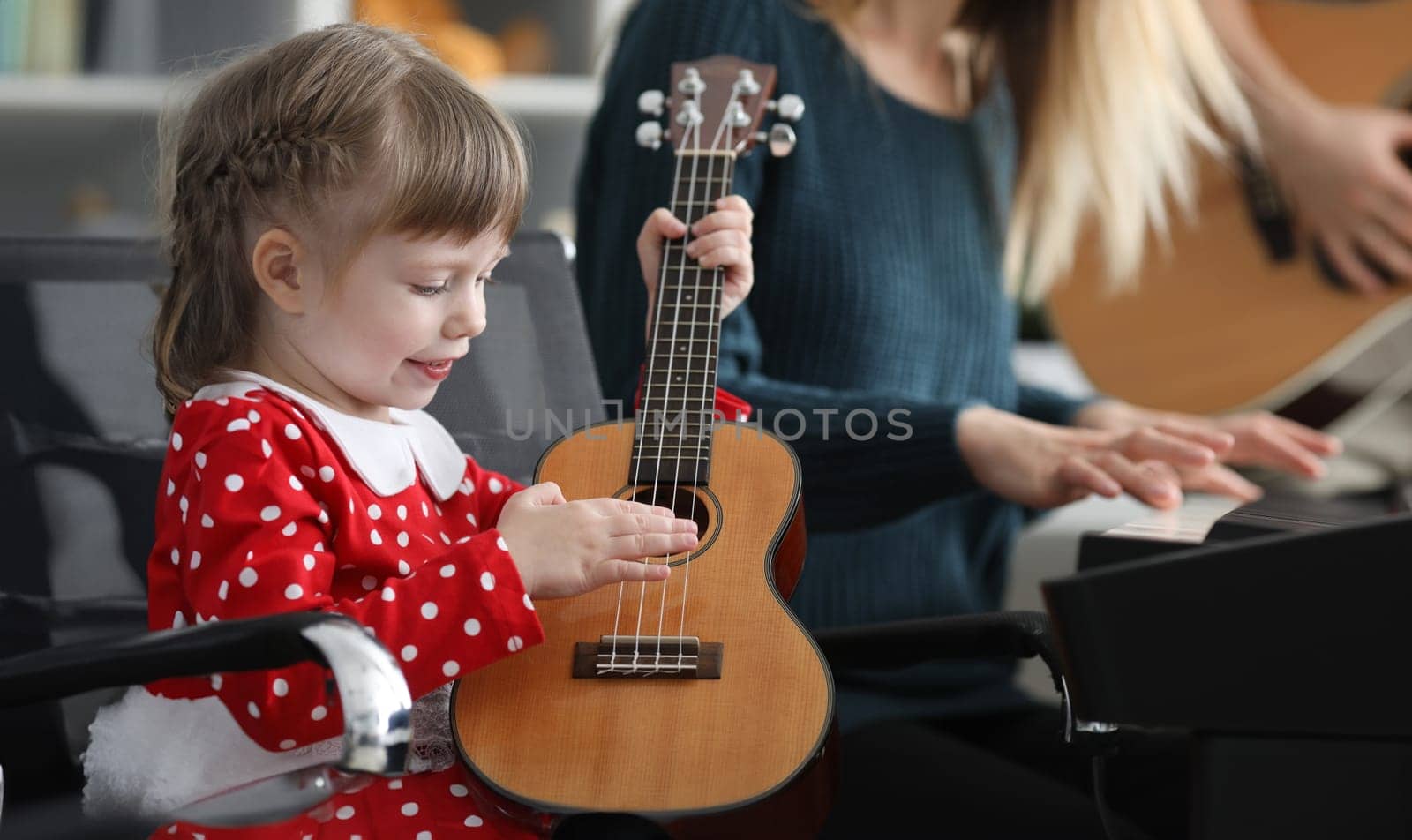 Happy little daughter plays ukulele near parents. Music is best way to success in life. Child learns to own musical instrument. Parents listen carefully to works performed by child