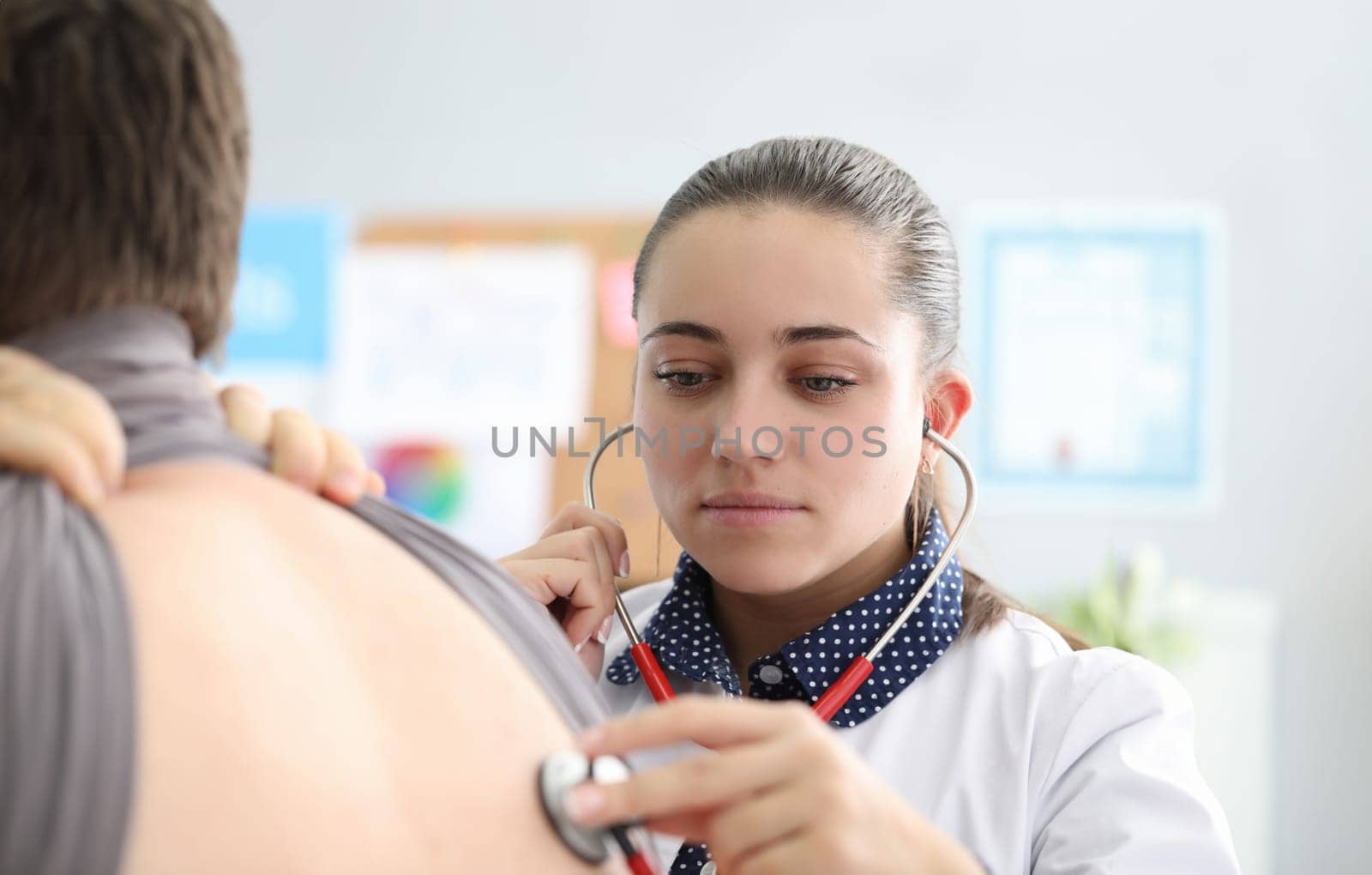 Woman therapist in clinic listens to lungs man by kuprevich