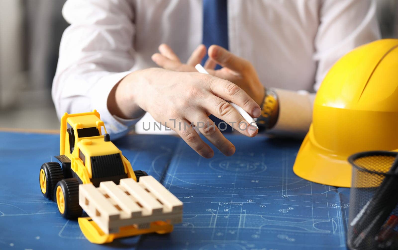Man holds pencil, on table yellow helmet and truck by kuprevich