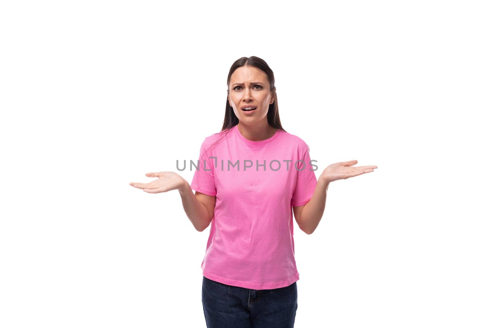 young slim brunette woman in pink basic t-shirt has doubts on white background with copy space by TRMK