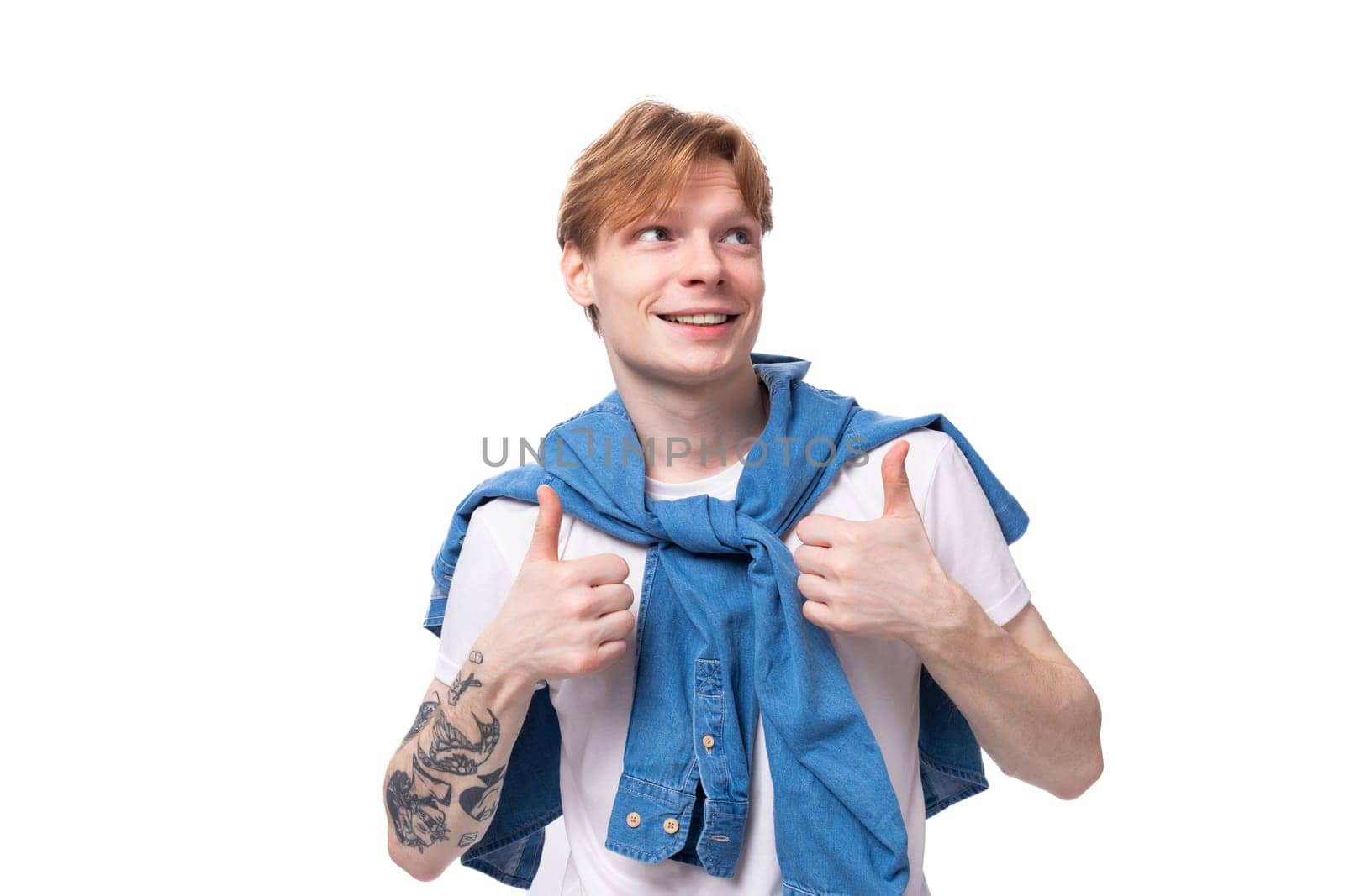 young fashionable caucasian guy with short red hair with a tattoo on his arms is dressed in a white t-shirt on a white background with copy space.
