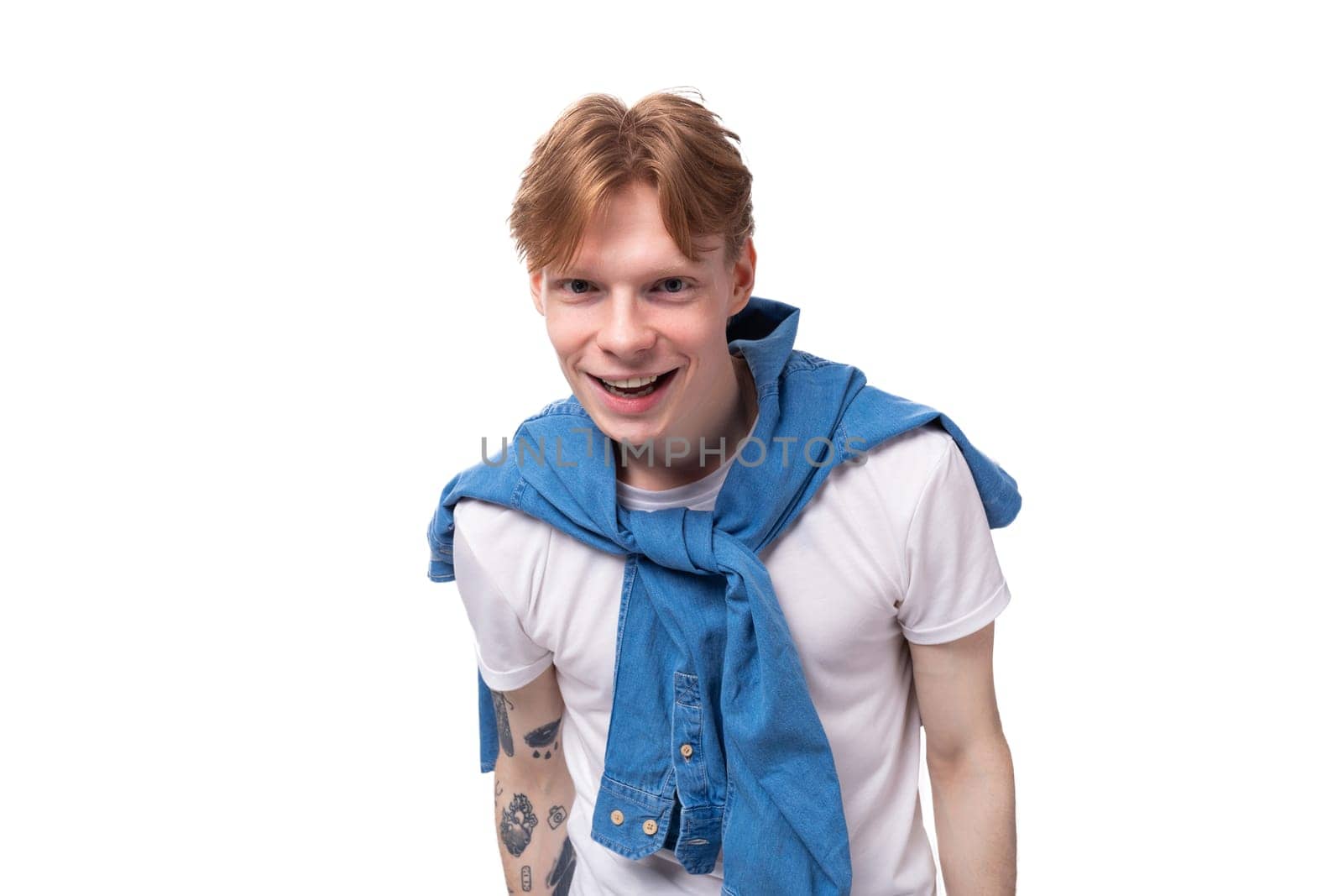 young charming slender red-haired man with a short haircut with a tattoo on his arms is dressed in a stylish blue shirt by TRMK