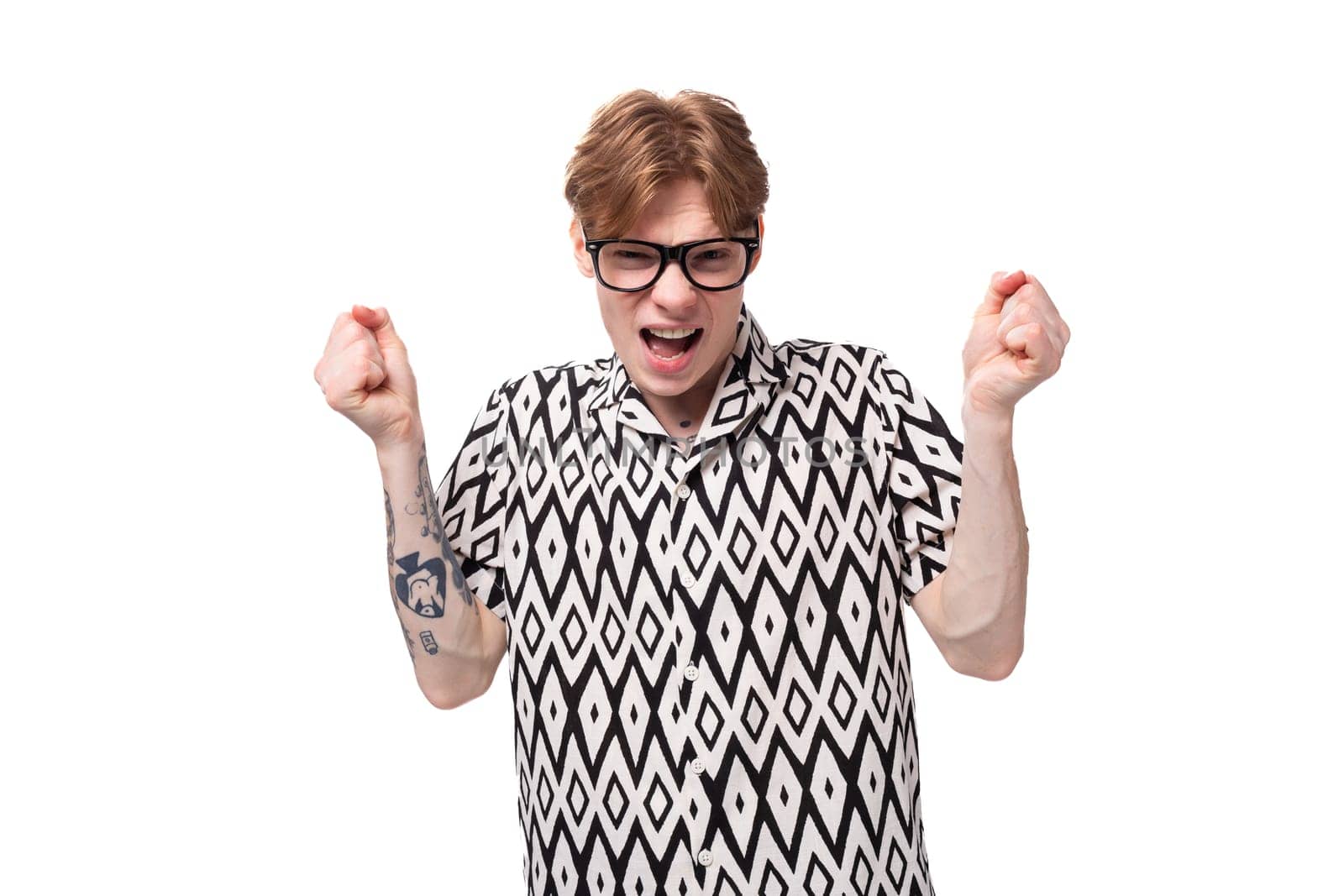 a young handsome man in glasses with red hair and a tattoo on his arms is dressed in a short-sleeved shirt.