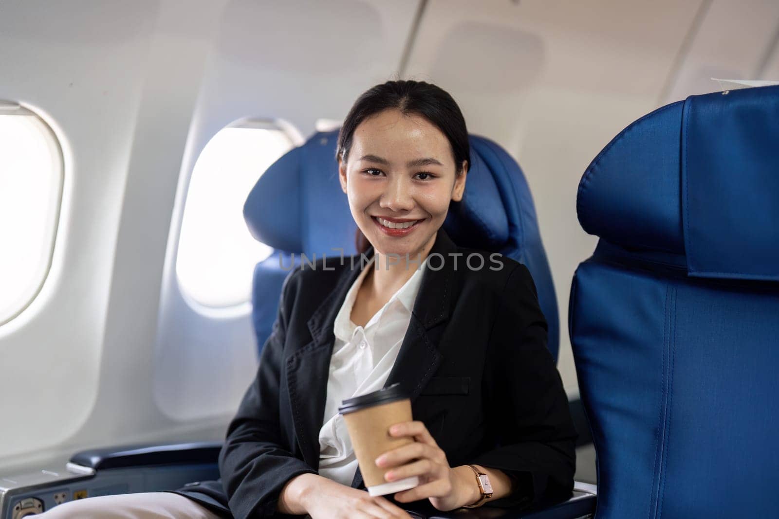 Portrait of A smiling successful Asian businesswoman or female entrepreneur in formal suit in a plane sits in a business class seat during flight.