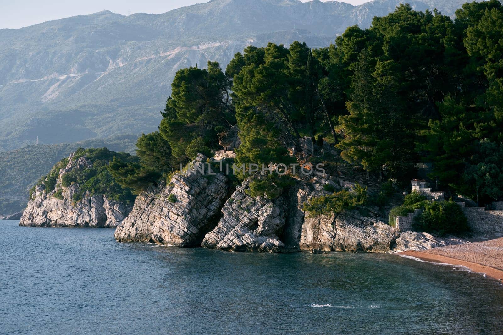 Sheer rocky seashore with green trees against the backdrop of mountains. High quality photo