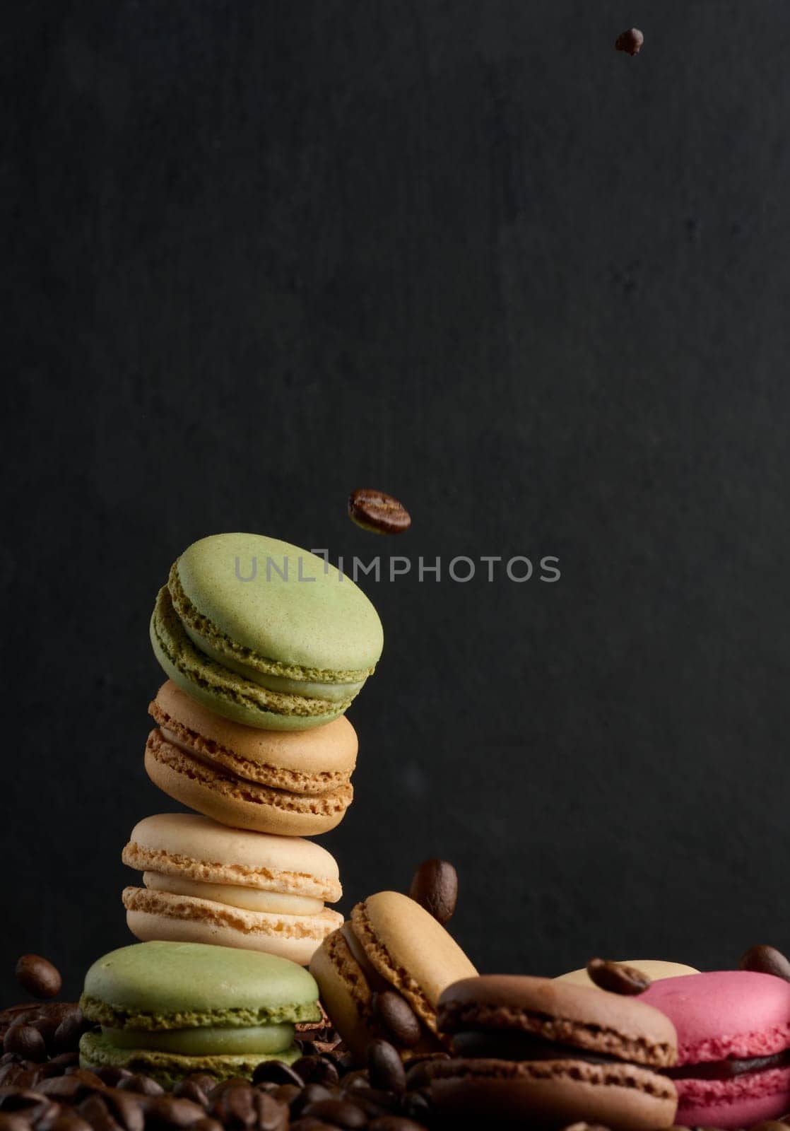 Stack of multi-colored macarons on a background of coffee beans, black background by ndanko