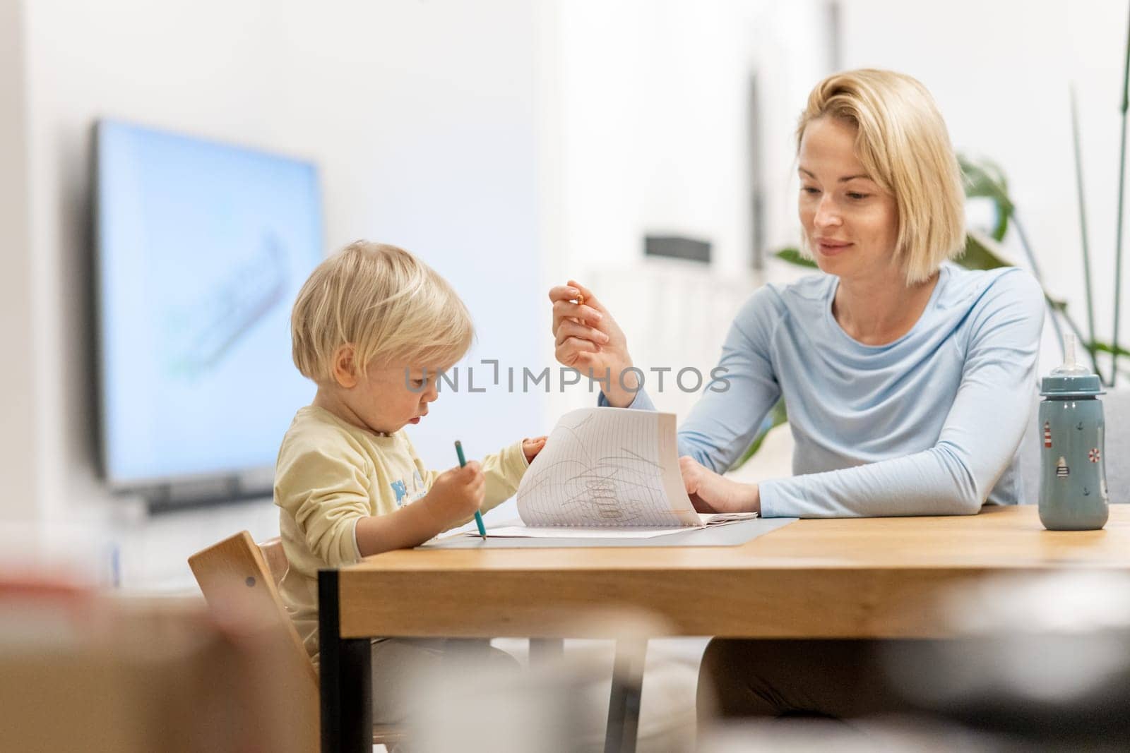 Caring young Caucasian mother and small son drawing painting in notebook at home together. Loving mom or nanny having fun learning and playing with her little 1,5 year old infant baby boy child