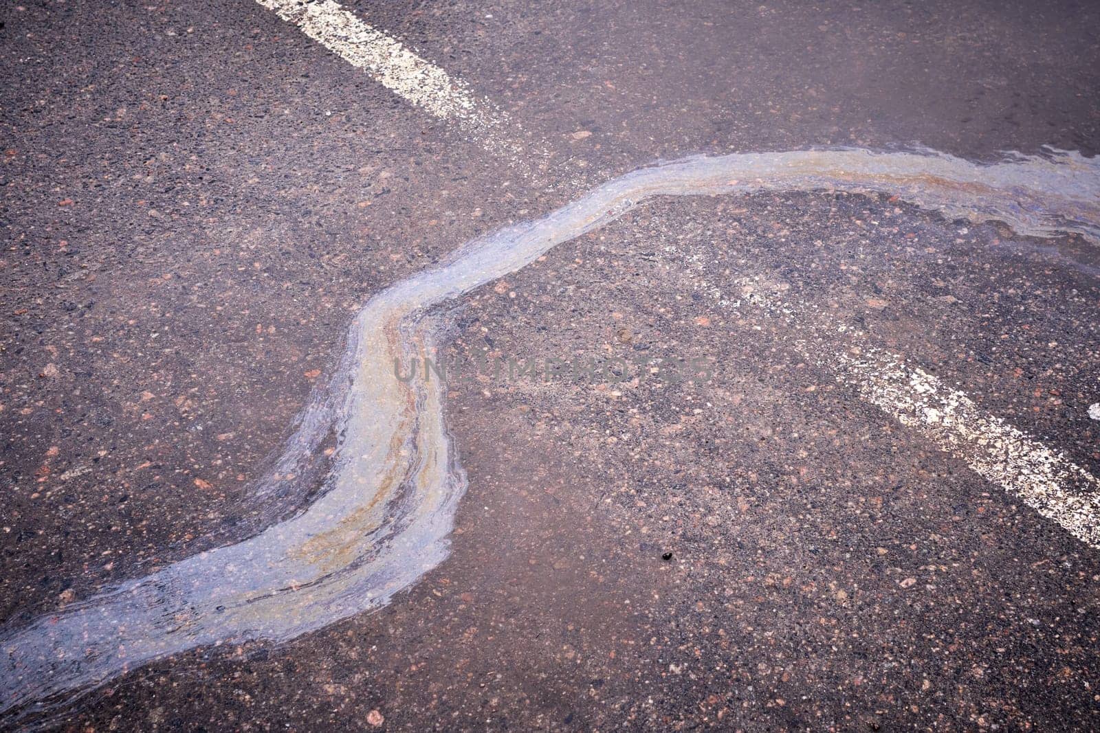 Oil, gasoline, or oil spill on wet asphalt with a parking lot and a dividing line. Water with patches of gasoline and oil.