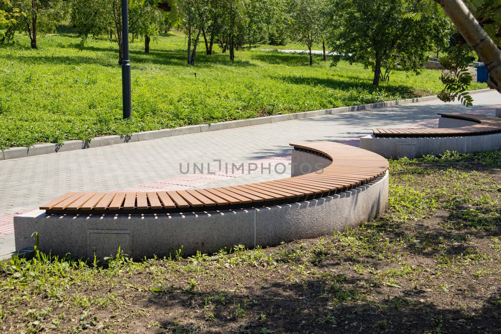 Close-up of a brown wooden bench in the shape of an arc in a summer city park.