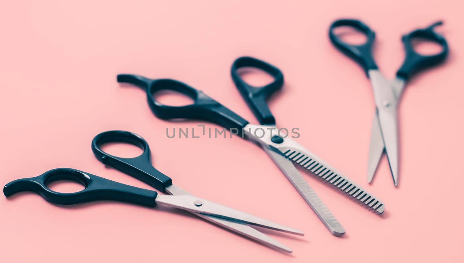 Set of three pairs of hairdresser's scissors on a pink background,close-up side view with depth of field. The concept of hairdressing, beauty salon, tools.