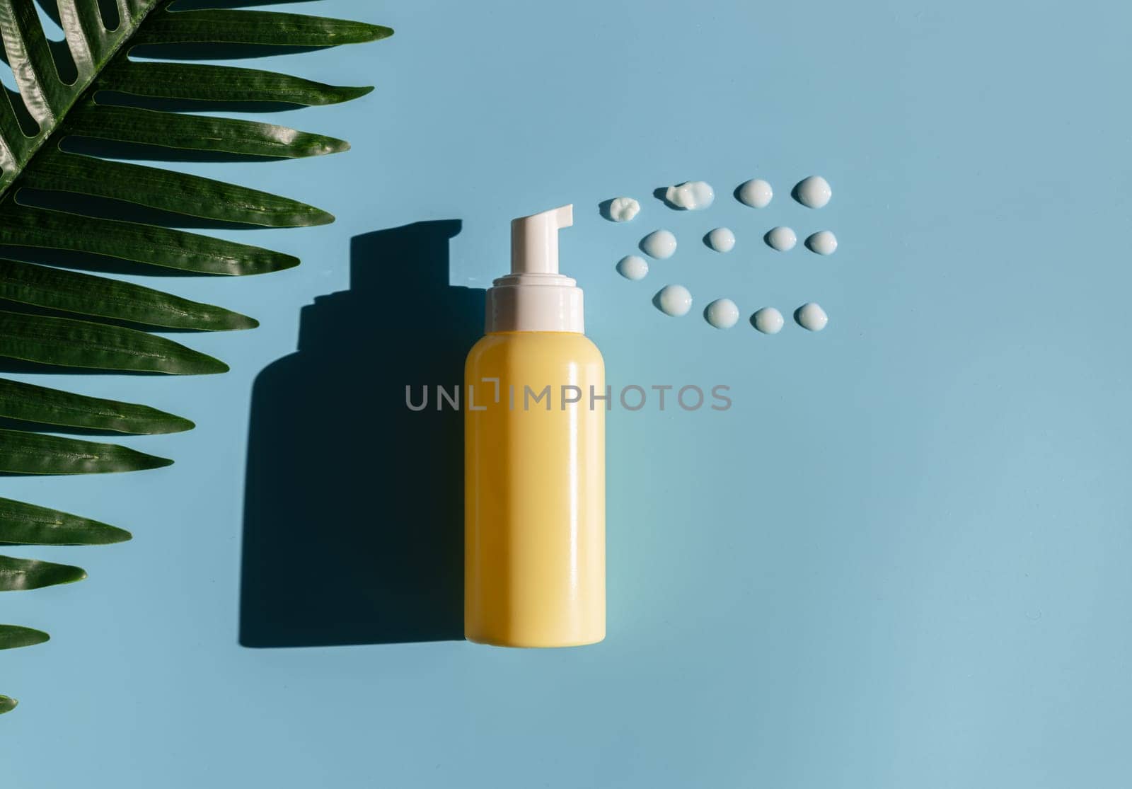 Yellow bottle with dispenser and drops of gel on a blue background. by Nataliya