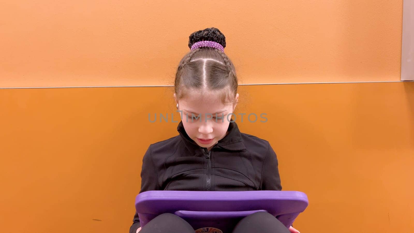 Nestled in a quiet hallway, this dedicated young figure skater finds a moment of tranquility, engrossed in her tablet as she mentally prepares for her upcoming performance.