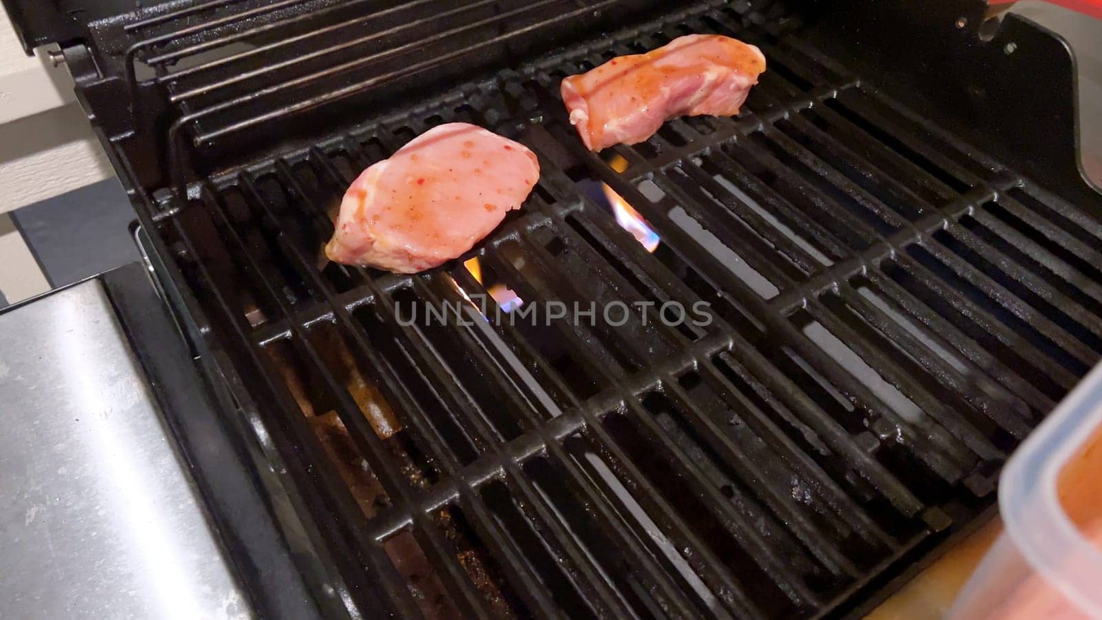 Fresh pork chops are graced with the perfect blend of seasoning as they cook to perfection, with hints of golden sear marks from the heat of an outdoor gas grill.