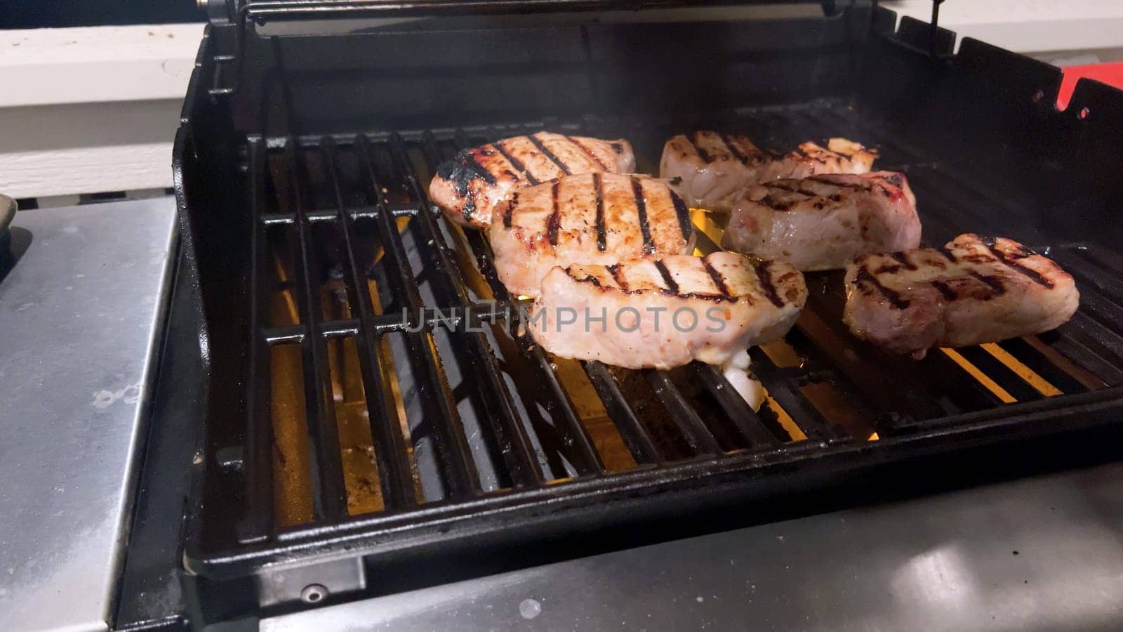 Fresh pork chops are graced with the perfect blend of seasoning as they cook to perfection, with hints of golden sear marks from the heat of an outdoor gas grill.