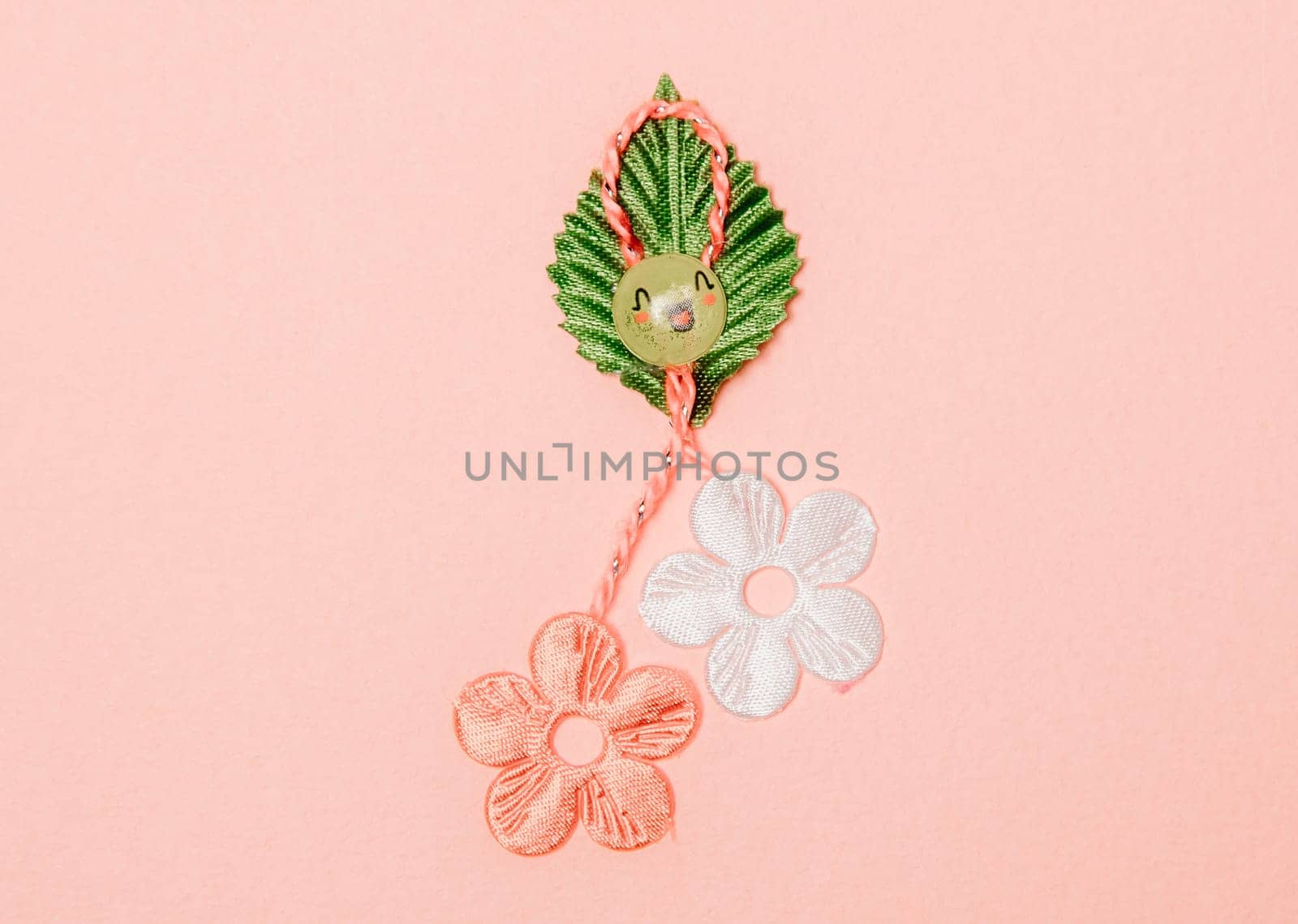 One beautiful homemade martisor made from flowers, a petal and a cheerful smiley face lies in the center on a pink background, flat lay close-up.