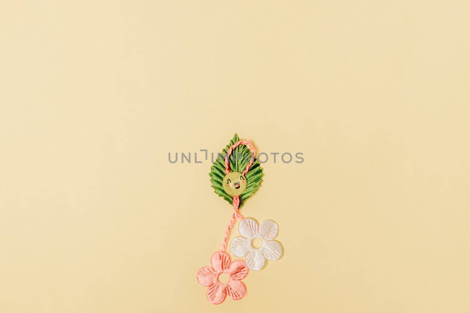 One beautiful homemade martisor made from flowers, a petal and a cheerful smiley face lies at the bottom in the center on a gentle yellow background with copy space on the sides, flat lay close-up.