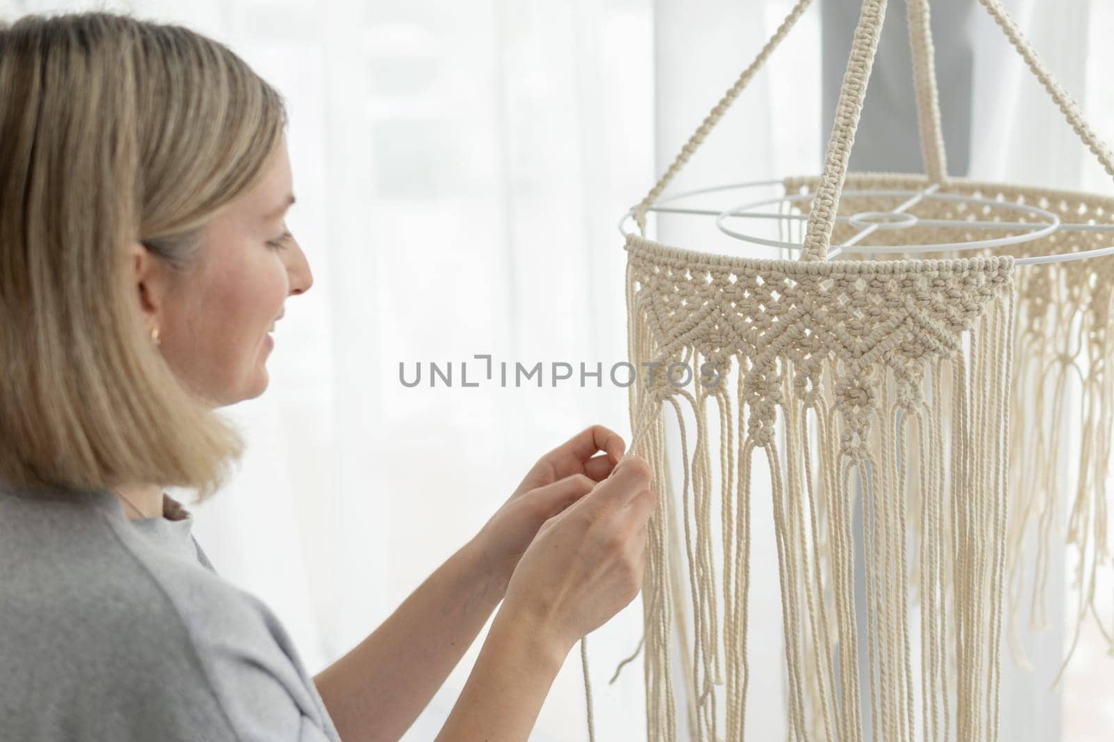 Closeup of middle-aged woman knits lampshade for interior using macrame technique. Happy woman knits boho chandelier