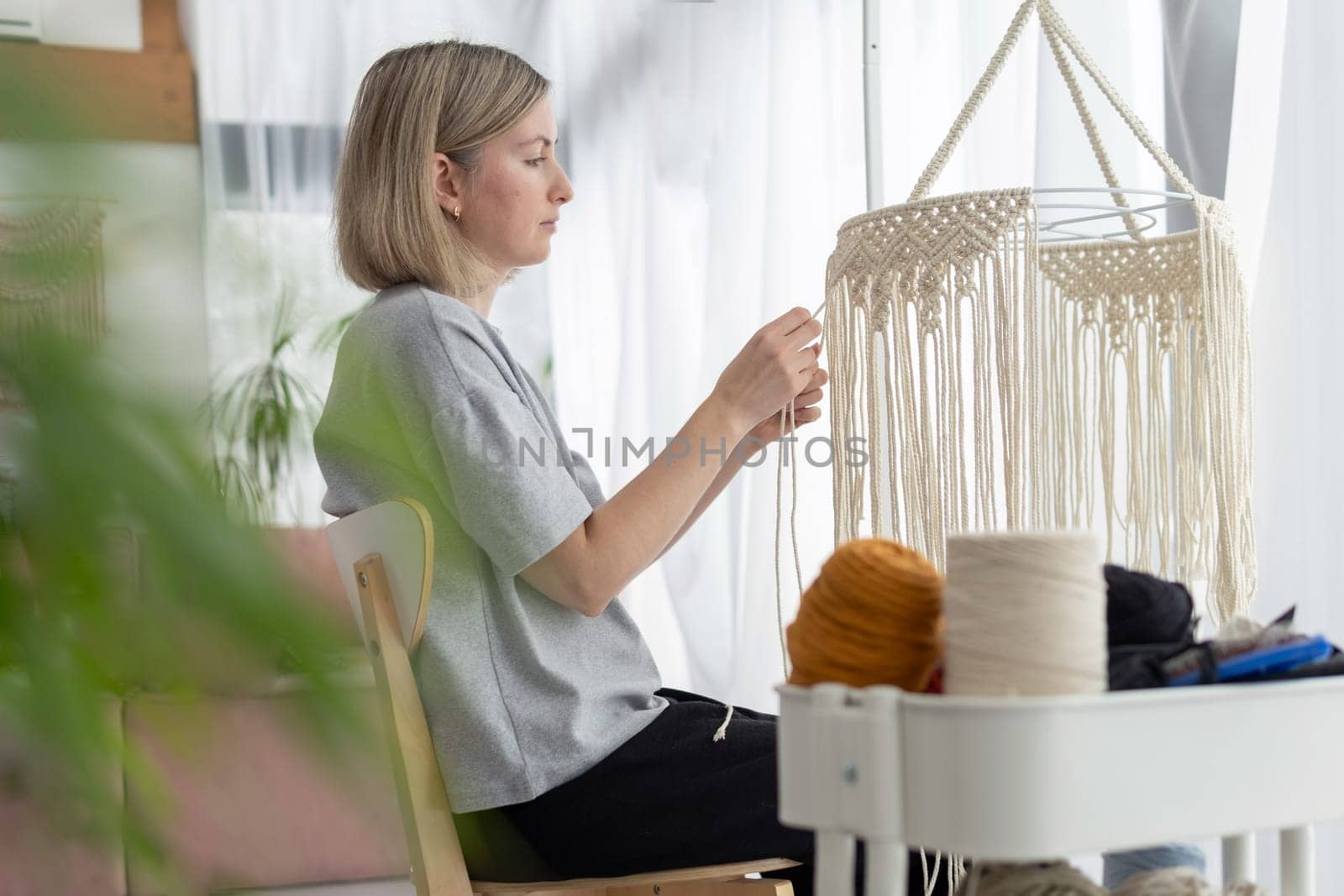 Middle-aged woman knits boho lampshade for interior using macrame technique. by dmitryz