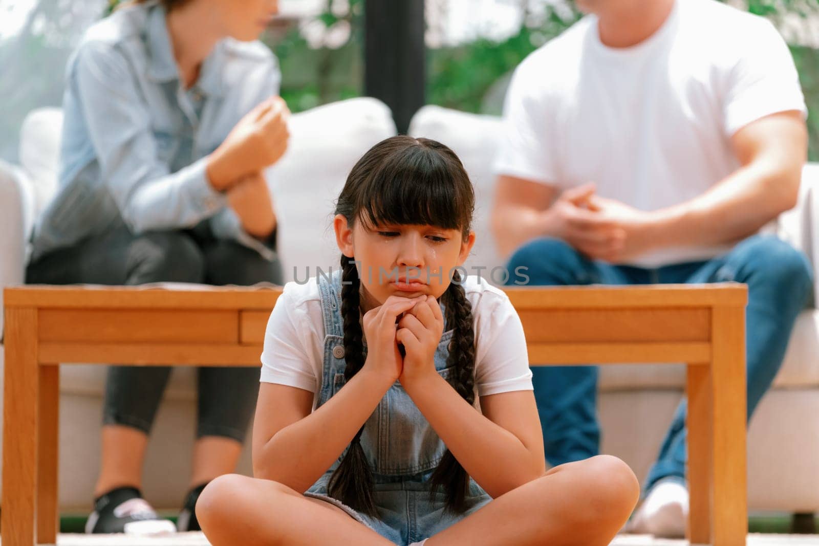 Stressed and unhappy young girl crying and trapped in middle of tension by her parent argument in living room. Unhealthy domestic lifestyle and traumatic childhood develop to depression. Synchronos