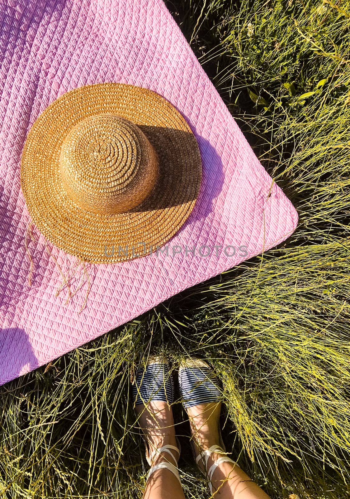 Summer flat lay. Picnic blanket, hat, woman legs on green grass. by AndriiDrachuk