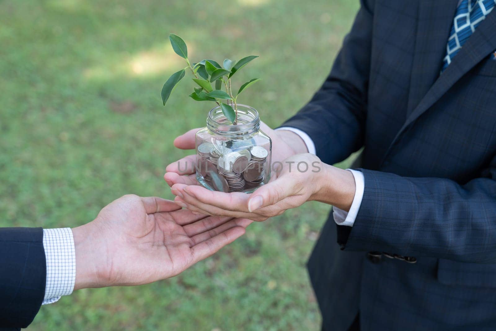 Concept of sustainable money growth investment with glass jar filled with money savings coins with businesspeople as eco-friendly financial investment nurtured with nature and healthy retirement. Gyre