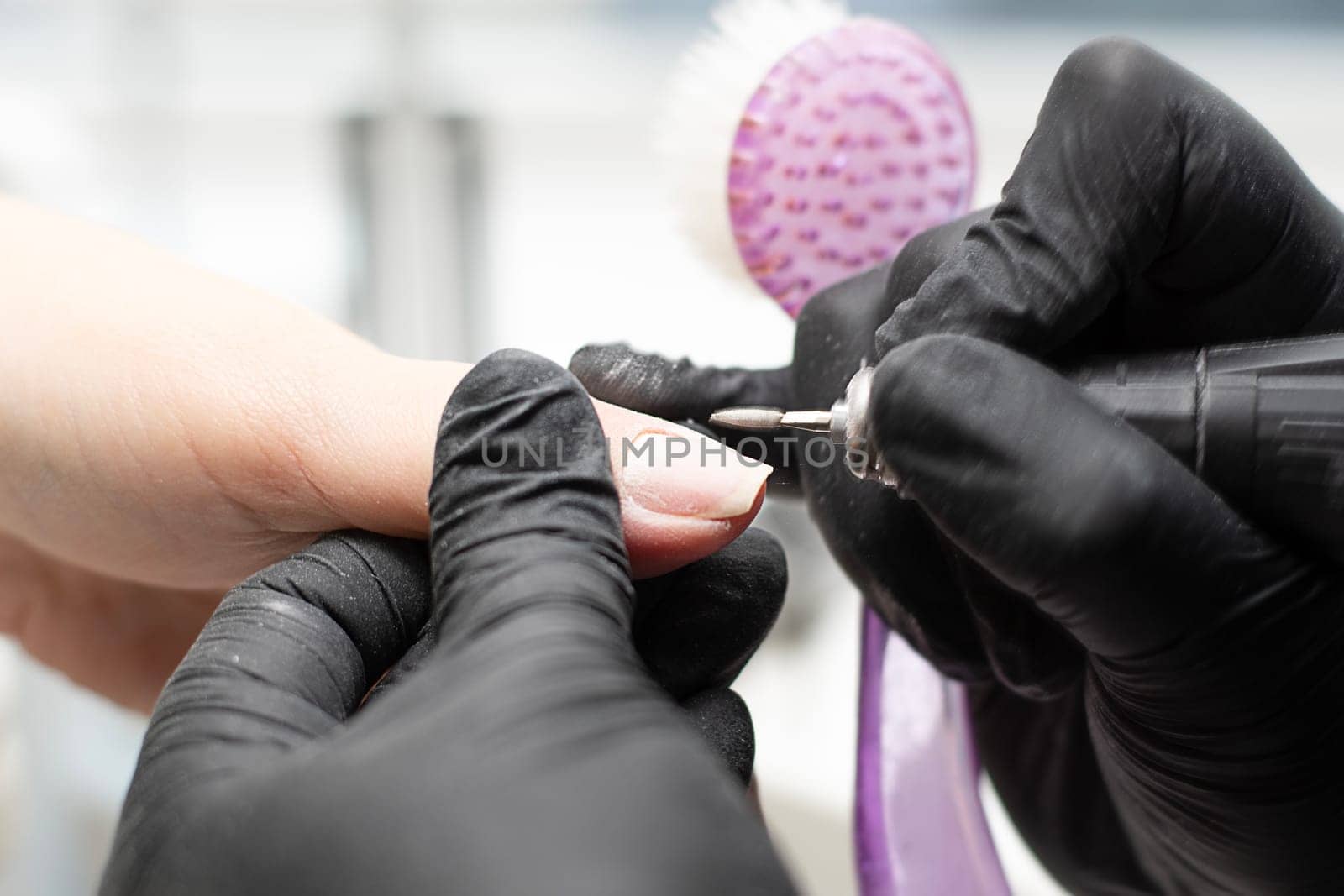 Beauty concept. A manicurist in black latex gloves makes a hygienic hardware manicure with a Fraser to a client in a beauty salon. Close-up. Horizontal.