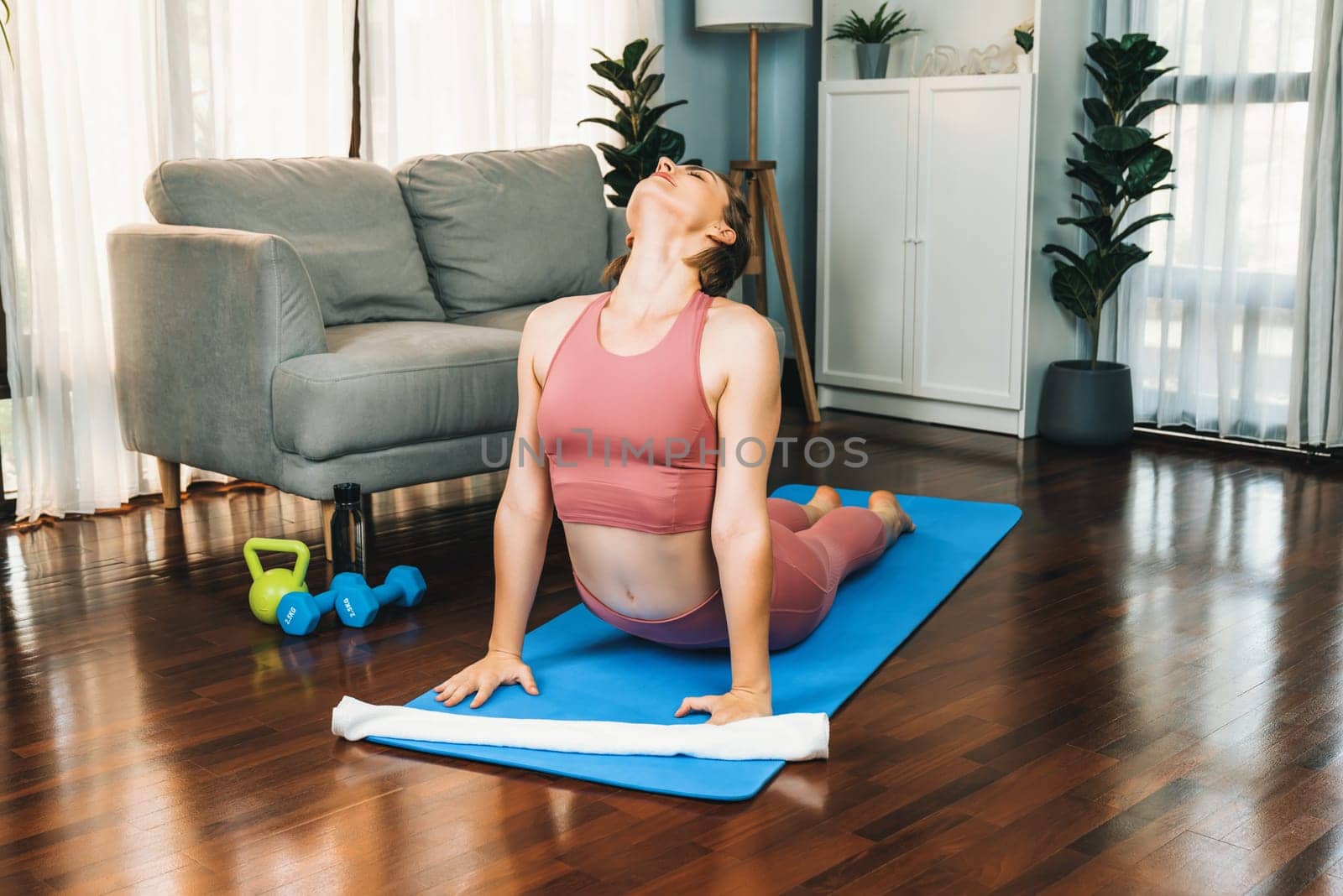 Flexible and dexterity woman in sportswear doing yoga position in meditation posture on exercising mat at home. Healthy gaiety home yoga lifestyle with peaceful mind and serenity.