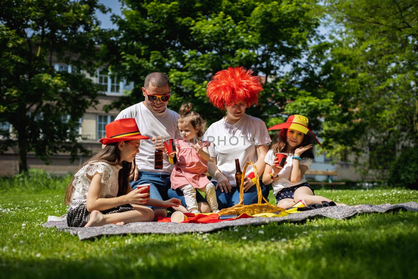 Portrait of beautiful and happy caucasian parents with three children girls celebrating belgium day at a picnic in a city park on a sunny summer day, close-up view from below.