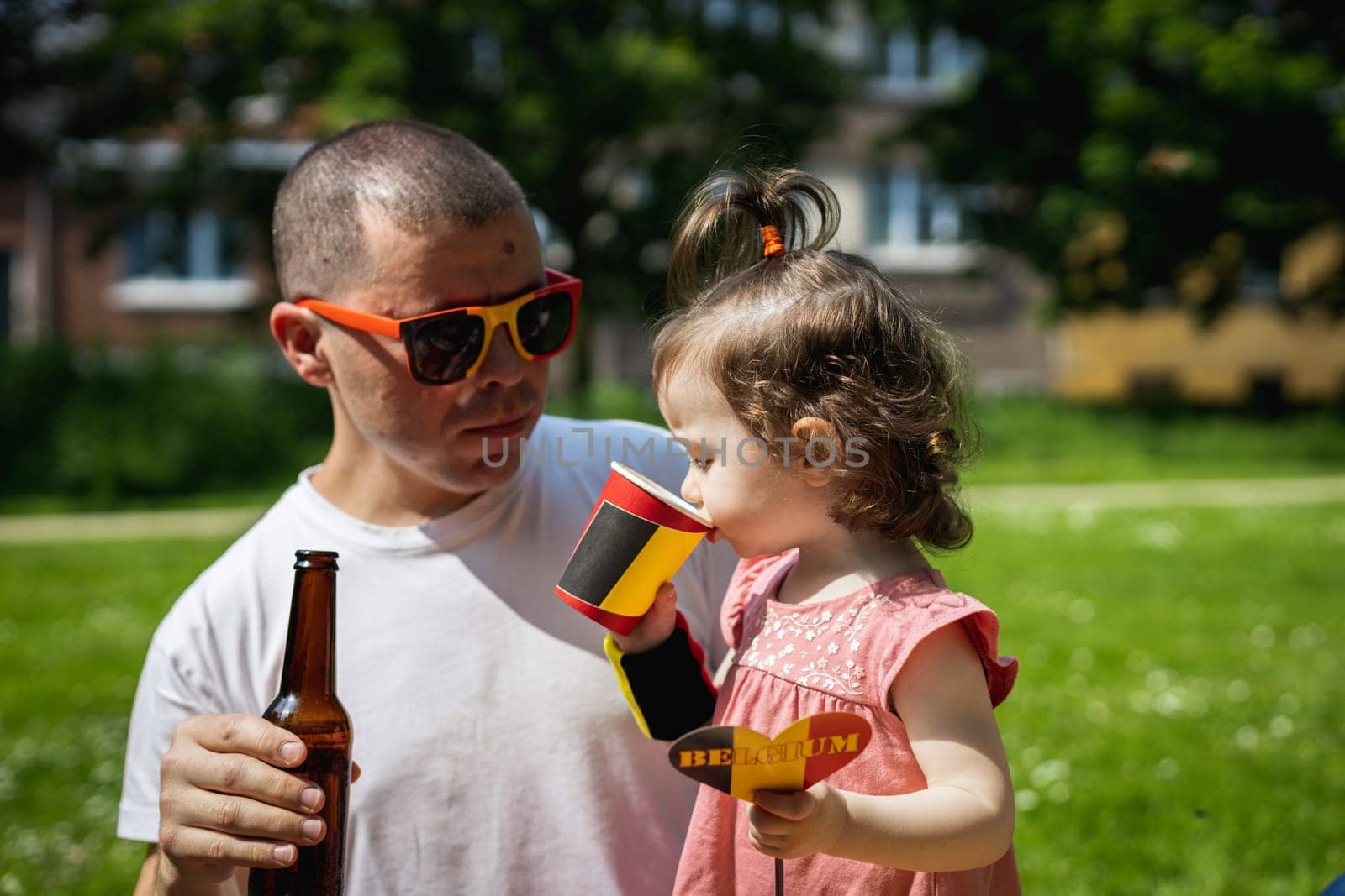 Portrait of dad and daughter drinking drinks and celebrating belgian day. by Nataliya