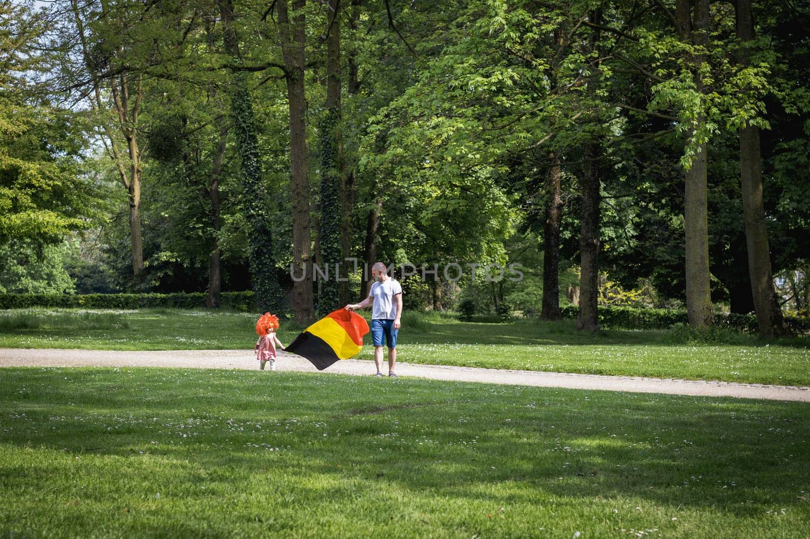 Portrait of a father with his daughter and the Belgian flag in the park. by Nataliya