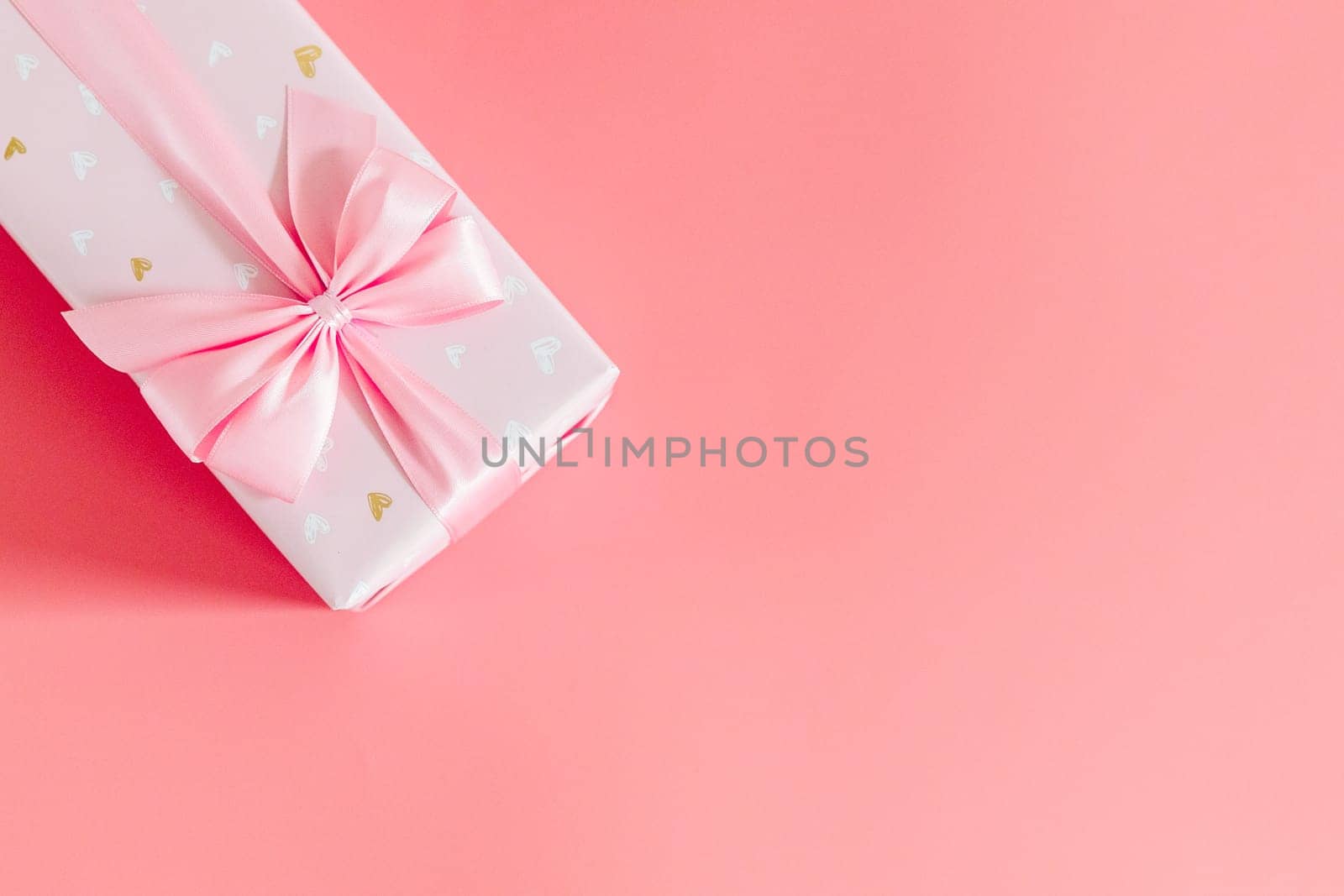 One beautiful gift box with a bow lie on the top left on a pale pink background with copy space on the right side, flat lay close-up.