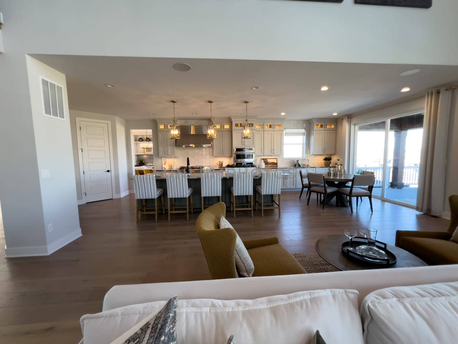 This spacious open-plan kitchen boasts white cabinetry, luxurious gold light fixtures, and a large island with stylish bar seating, ideal for family gatherings and entertaining guests.
