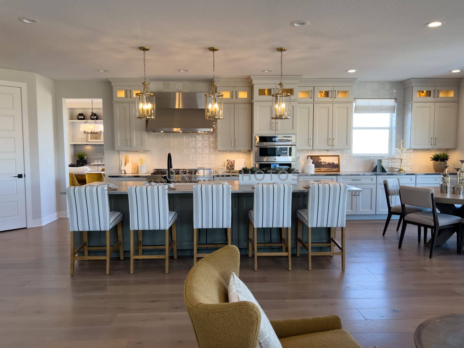 This spacious open-plan kitchen boasts white cabinetry, luxurious gold light fixtures, and a large island with stylish bar seating, ideal for family gatherings and entertaining guests.