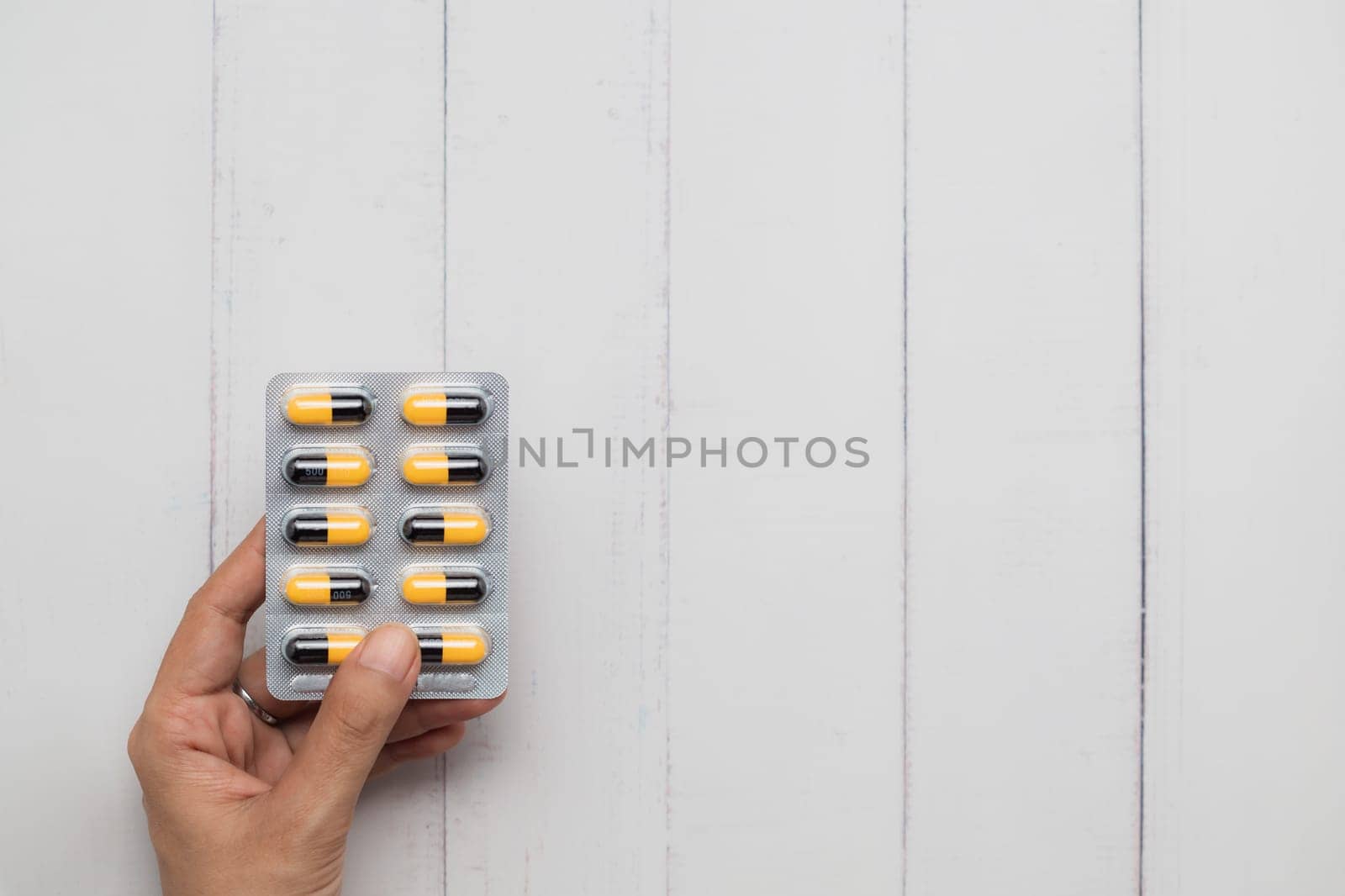A person holding a blister pack of yellow and black capsules on a white table. It appears to be Amoxicillin, an antibiotic medication for healthcare and medical concept.