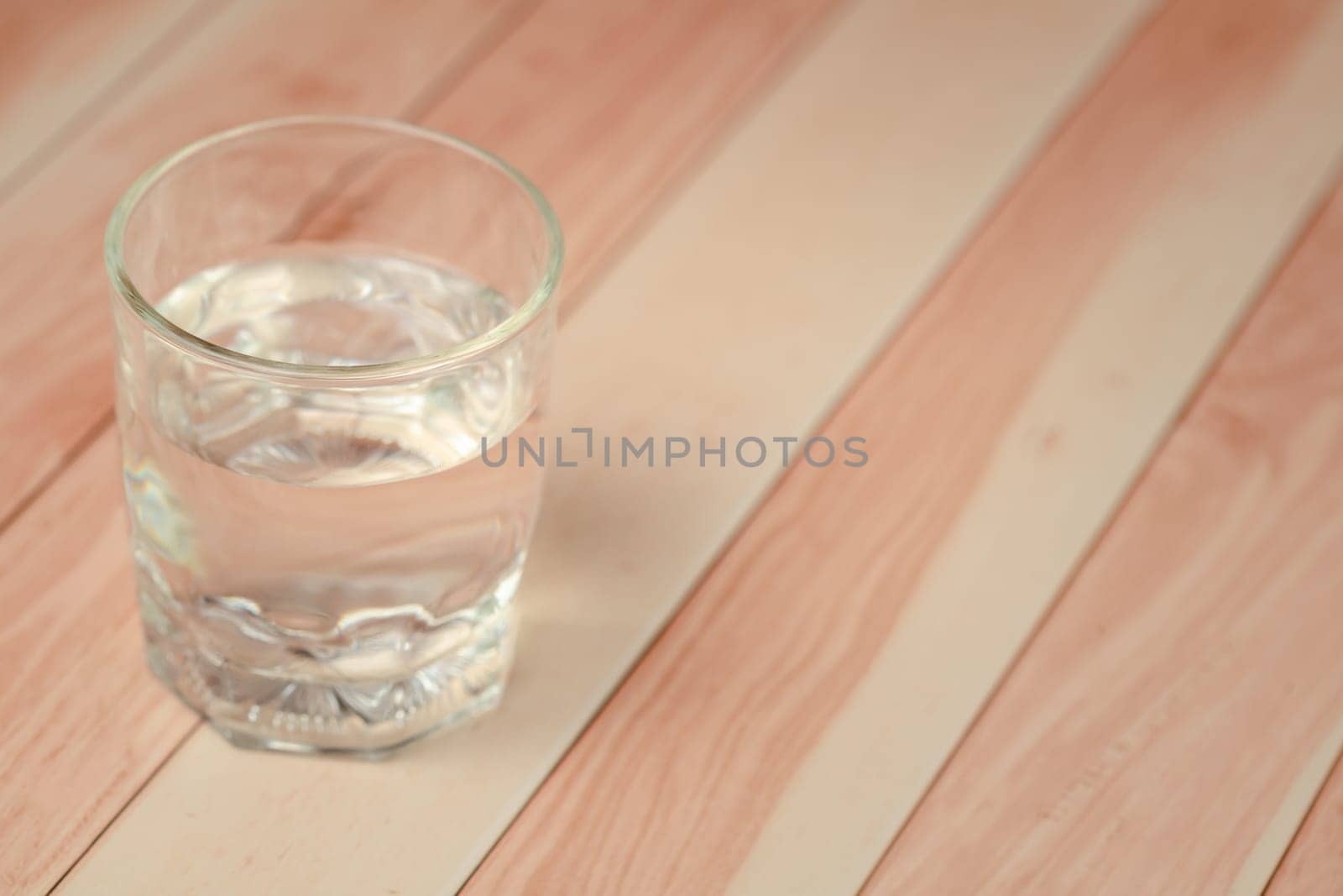 A clear glass filled with water on a wooden table for a refreshing and health-conscious beverage. Soft focus image.