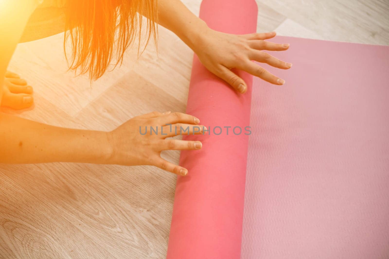 A young woman rolls a pink fitness or yoga mat before or after exercising, exercising at home in the living room or in a yoga studio. Healthy habits, keep fit, weight loss concept. Closeup photo.