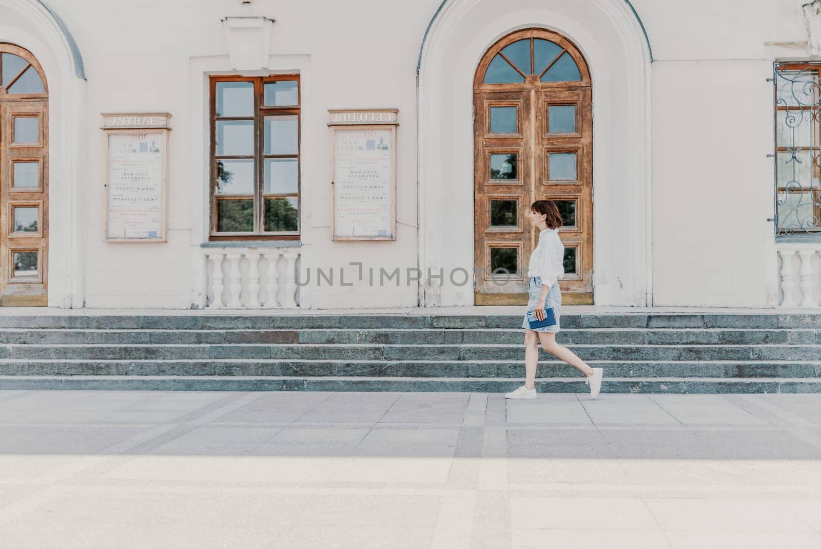 Woman staircase city. A business woman in a white shirt and denim skirt walks down the steps of an ancient building in the city.