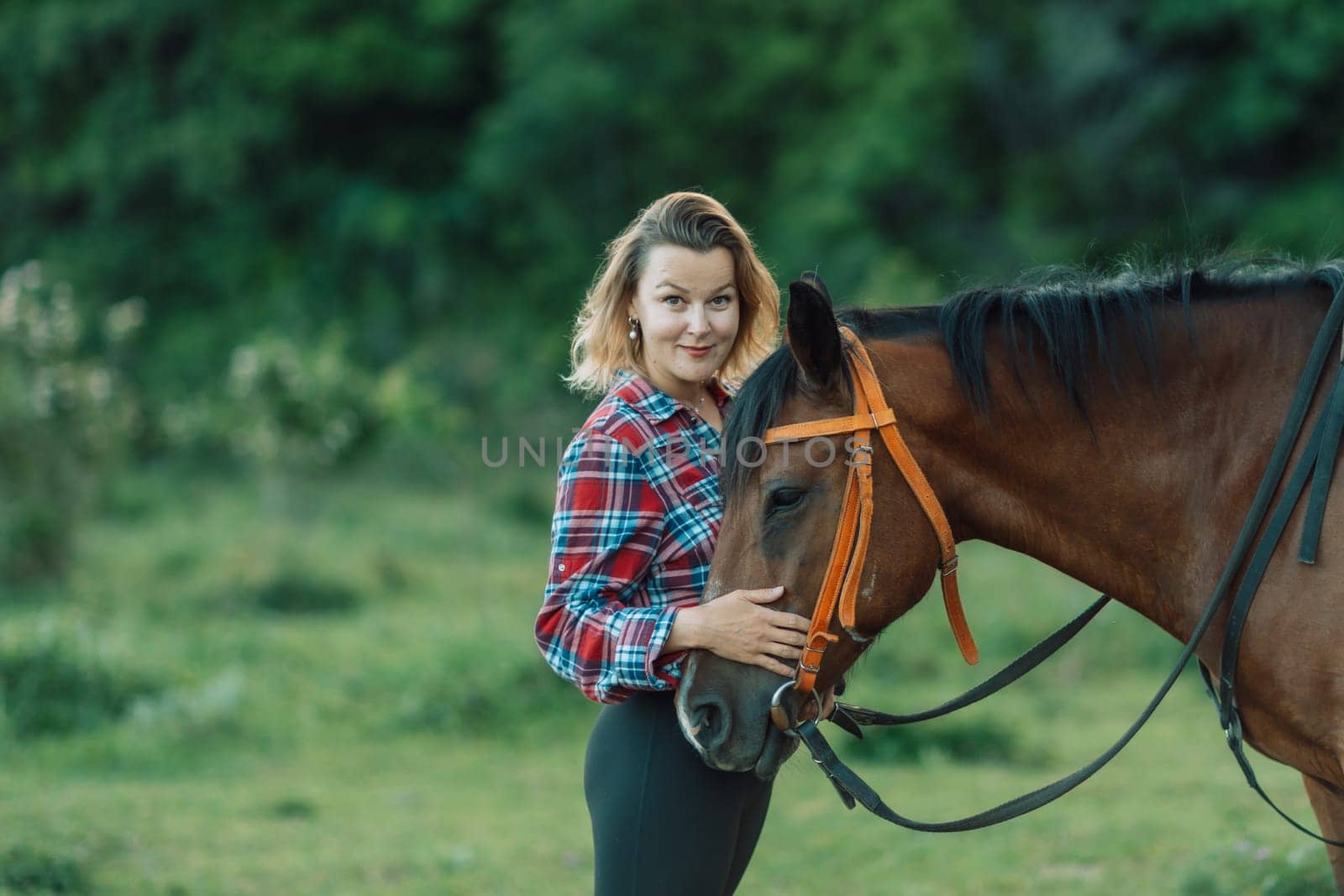 Happy blonde with horse in forest. Woman and a horse walking through the field during the day. Dressed in a plaid shirt and black leggings. by Matiunina