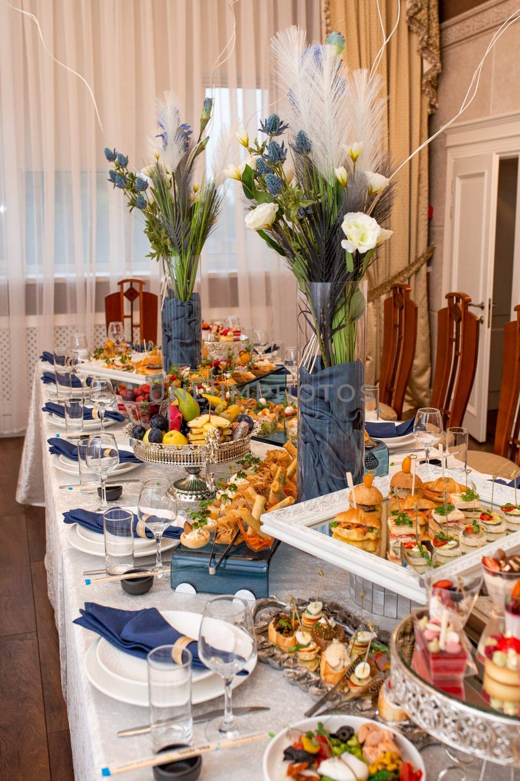 Opulent buffet with snacks, sandwiches, fruits, sweets on decorated table with blue accents. by Pukhovskiy