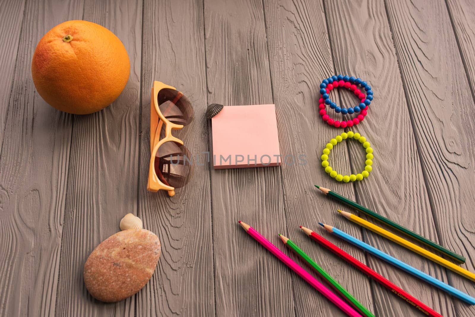 artist pencils for inscription. accessories sunscreen spf care. sunglasses bracelets orange fruit pebbles. Summer background template mockup space colorful composition text. Top view wooden background