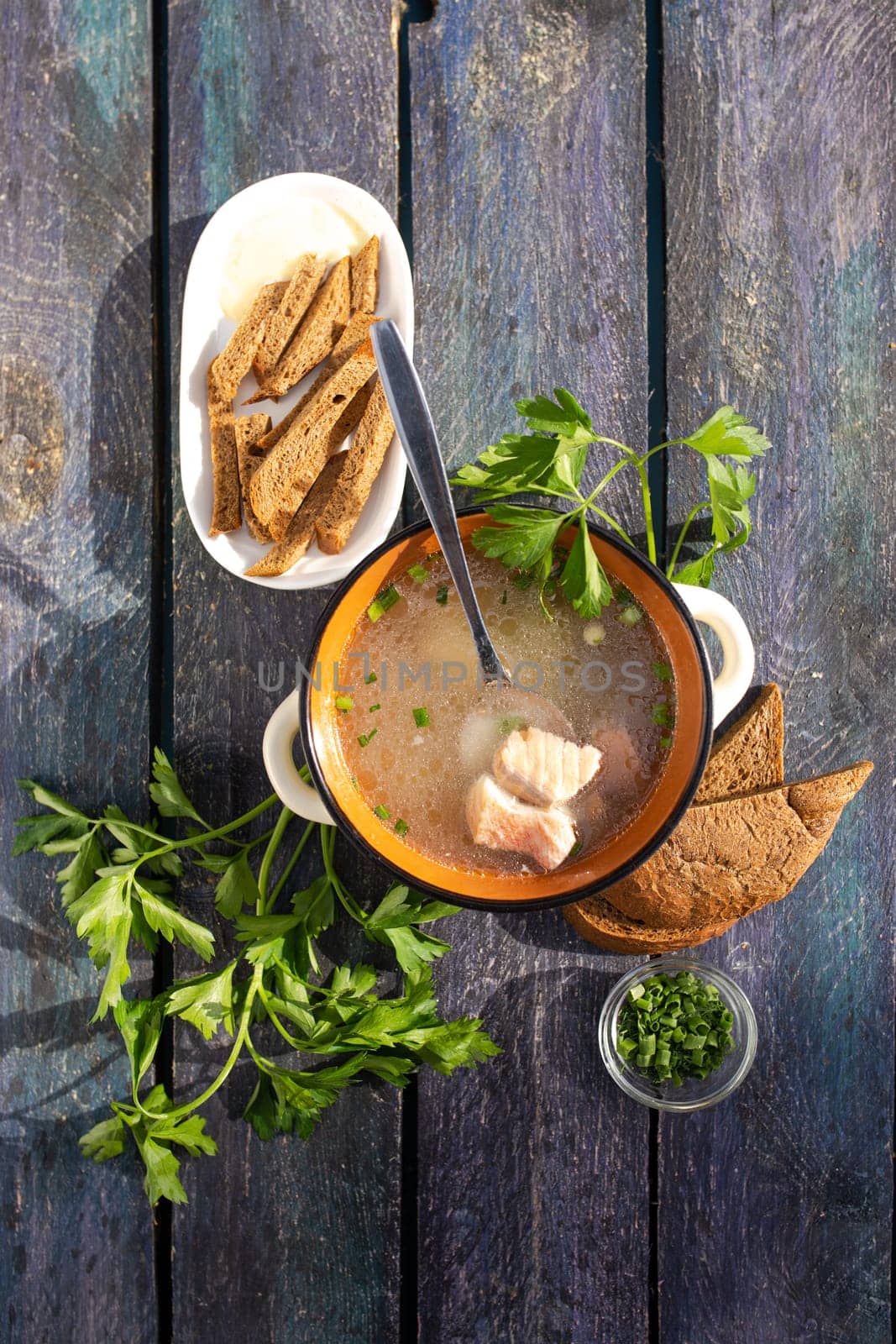 Close-up of a bowl of fish soup with fresh herbs and bread on a wooden table. by Pukhovskiy