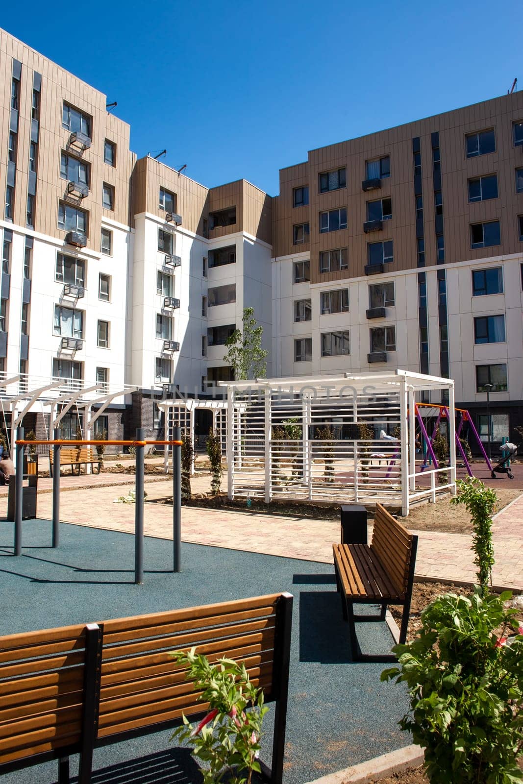 Modern apartment buildings with a courtyard playground. Contemporary design, large windows, balconies. Playground with swings, slide, climbing frame.