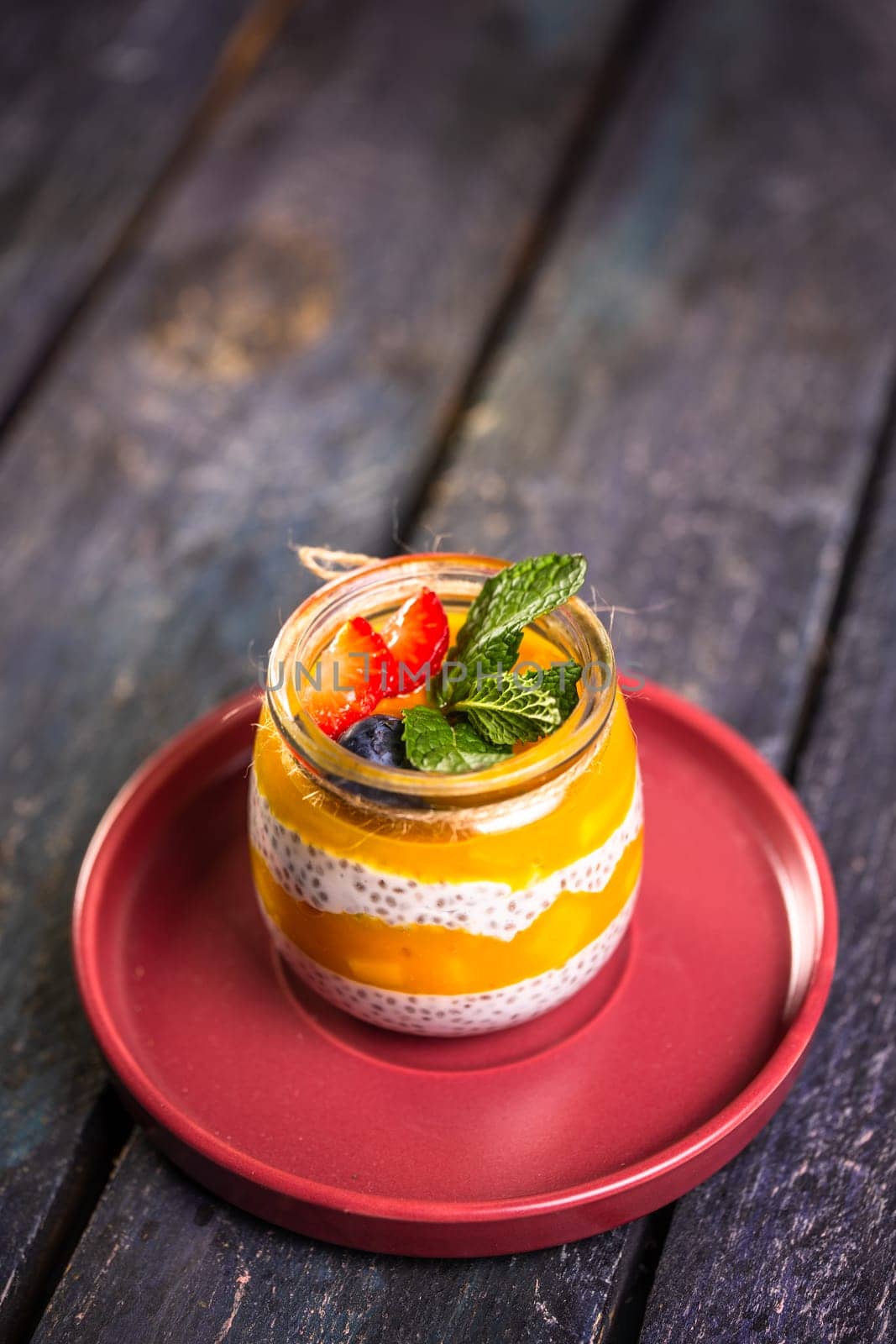 Chia Seed Pudding with Mango and Berries in Glass Jar on Red Plate by Pukhovskiy