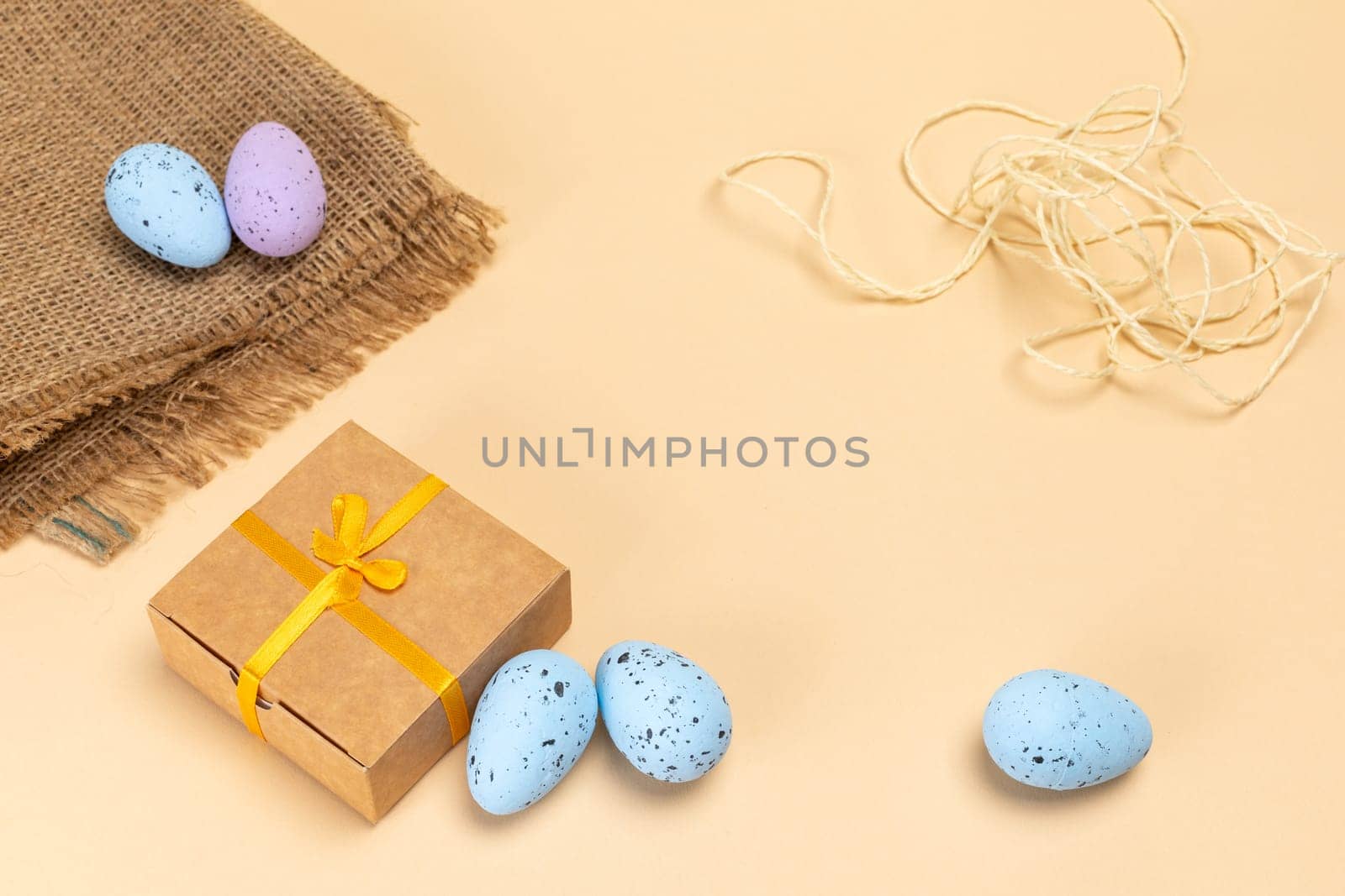 Colored Easter eggs on a sackcloth bag, a rope and a gift box. Top view.