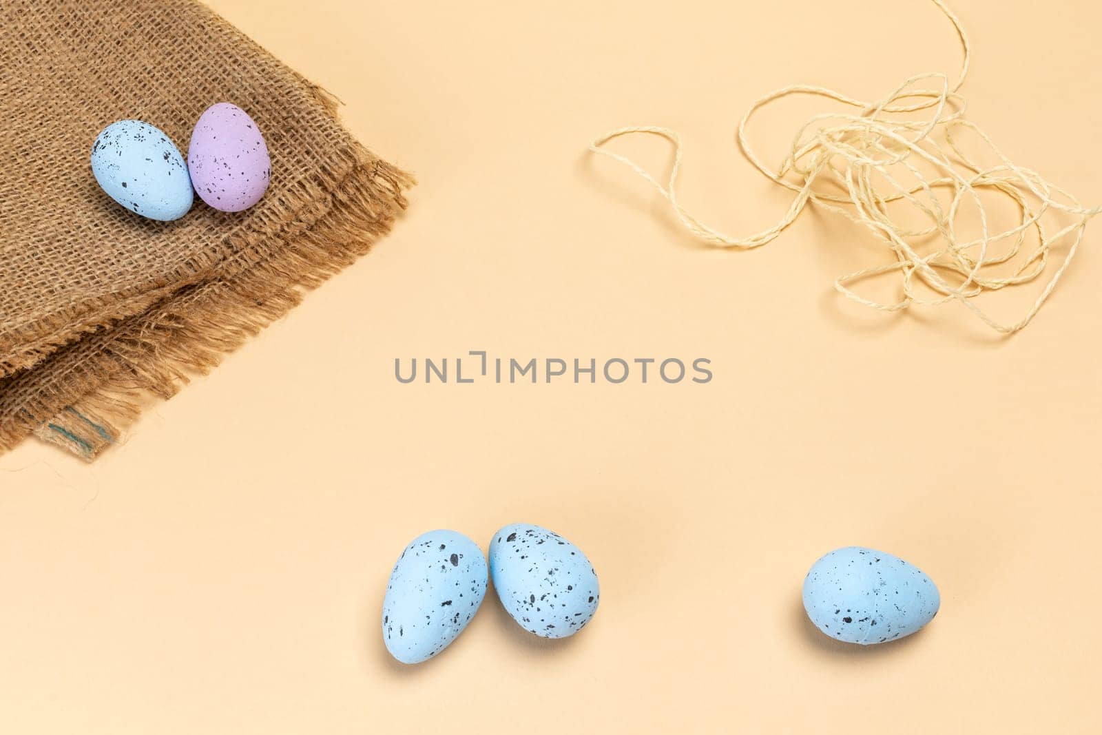 Colored Easter eggs with a sackcloth bag and a rope on the beige background. Top view.